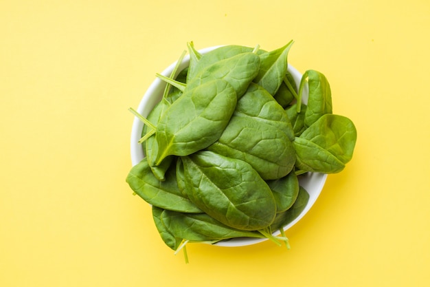 Fresh spinach leaves in a plate on a yellow background.