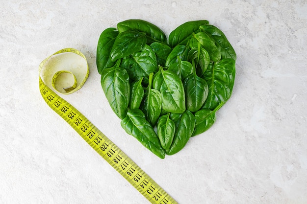 Fresh spinach leaves in the shape of a heart and a centimeter tape.