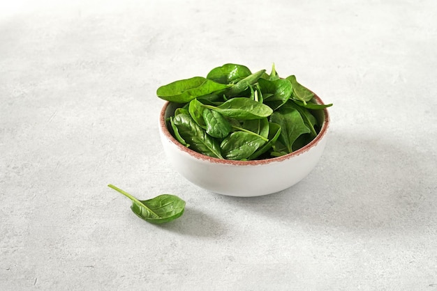 Fresh spinach leaves with water drops in ceramic bowl and cutting desk on the light background