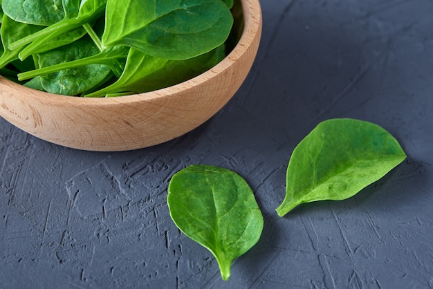 Spinaci freschi foglie in una ciotola di legno su uno sfondo scuro. cibo organico