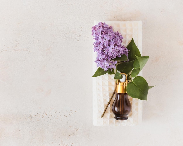 Fresh sprig of lilac and bottle with cosmetic oil on a white towel on light background spa concept