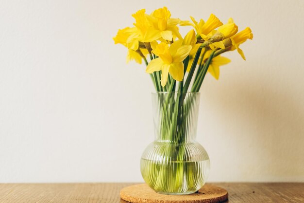 Fresh spring daffodils in vase on wooden table