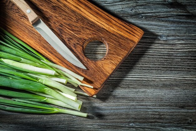 Fresh spring green onions stems kitchen knife wooden chopping board on vintage wood background