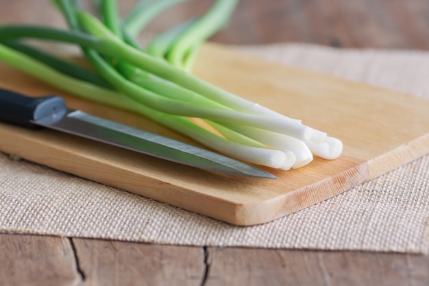 Foto la cipolla ed il coltello da cucina freschi della molla hanno messo il tagliere di legno sulla tavola di legno.