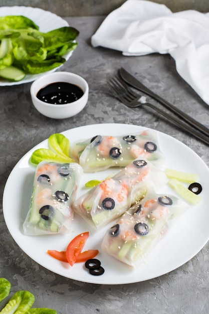 Fresh spring rolls in rice paper made from shrimp olives and vegetables on a plate Vertical view