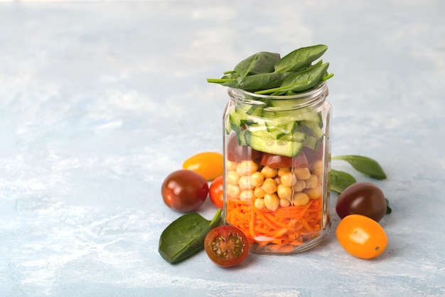 Fresh spring salad of carrots, chickpeas,tomato, cucumbers and spinach in a glass jar for a snack with you. The concept of healthy proper nutrition for the whole family. selective Focus