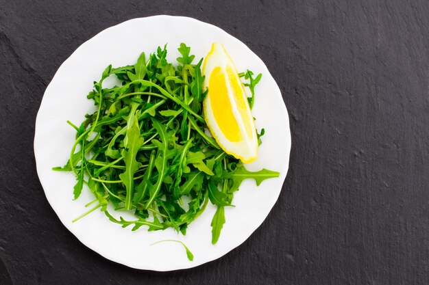 Fresh spring salad with rucola and lemon, in bowl on dark stone background with free text space.