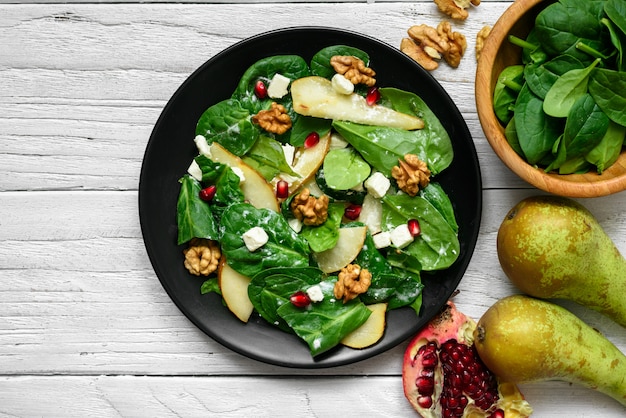 Fresh spring salad with spinach leaves, pear, nuts, pomegranate and feta cheese in black plate