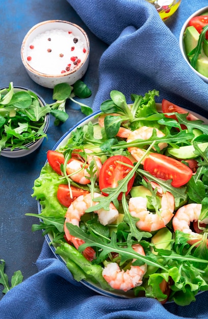 Fresh spring shrimp salad with tomatoes arugula avocado and\
olive oil lemon dressing blue table background top view copy\
space