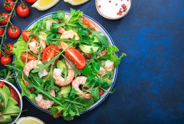 Fresh spring shrimp salad with tomatoes arugula avocado and olive oil lemon dressing blue table background Top view copy space