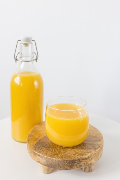 Fresh squeezed orange juice in bottle and glass on wooden tray on table white background Healthy beverage for breakfast Side view copy space