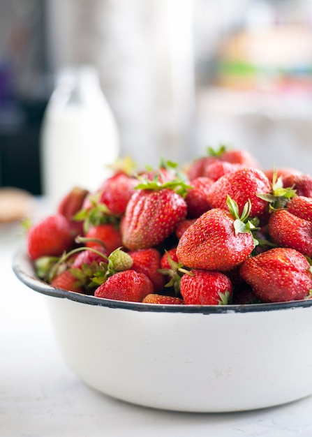 Fresh strawberries in a bowl and bottle of milk.