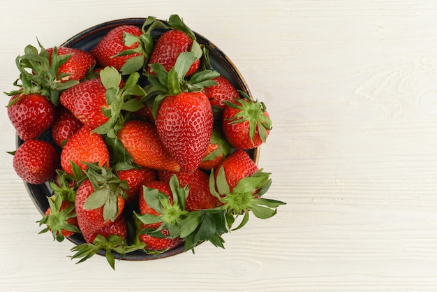 Fresh strawberries in a bowl on white wooden table. Top view. Copy space. Berries background. Beautiful red strawberry.