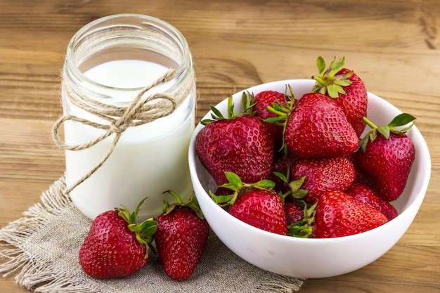 Fresh strawberries in a bowl with a bottle of milk on the table