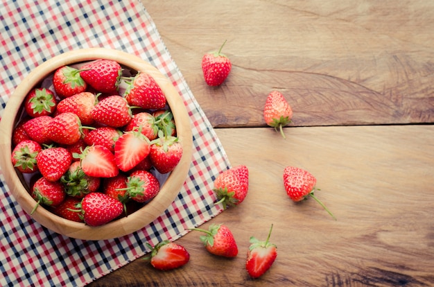 Fresh strawberries in a bowl on wooden background.