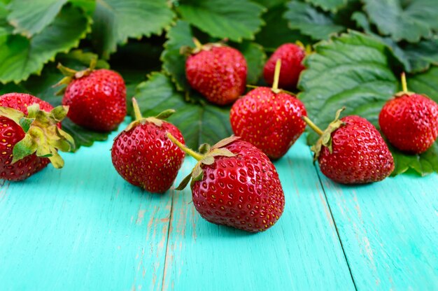 Fresh strawberries and green leaves on a wooden background.