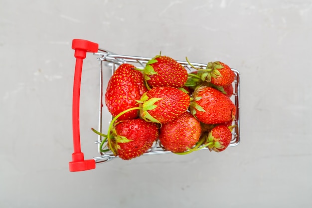 Fresh strawberries in a grocery cart on a gray background. Horizontal photo