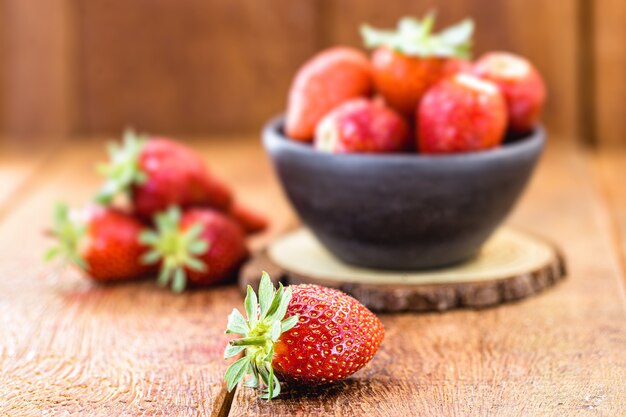 fresh strawberries in handmade clay bowl with wooden background and copy space