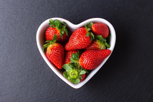 Fresh strawberries in heart bowl Sweet red berries on dark background Healthy and organic dessert