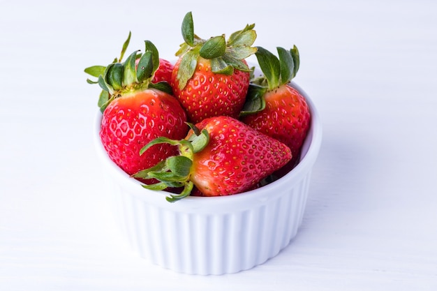 Fresh strawberries inside the white ramekin on the white wooden background