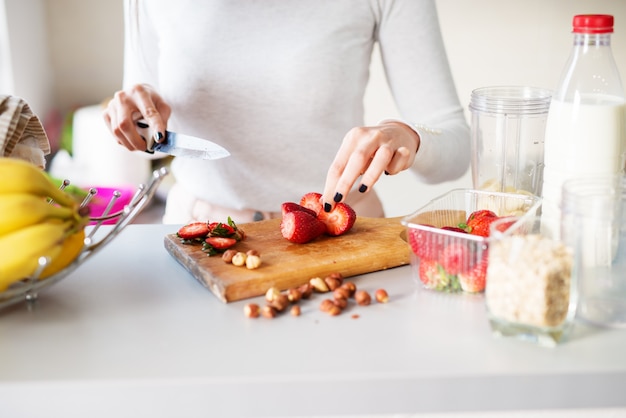 Fresh strawberries straight out of garden are being cut by a woman on a bright kitchen desk.