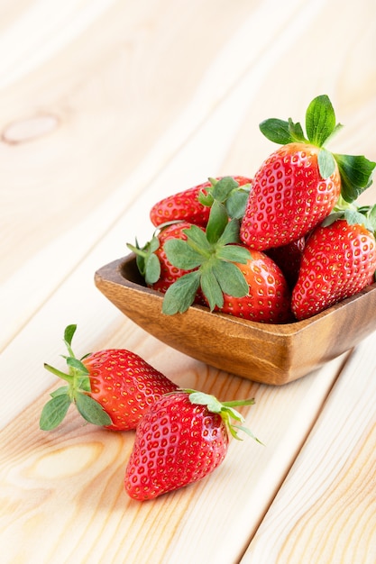 Fresh strawberries in wooden bowl on brown vintage table. Red juicy strawberry on wooden background. Close up.