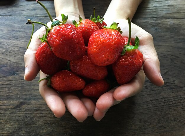 Fresh strawberry background. Ripe strawberry in woman hands against wood table