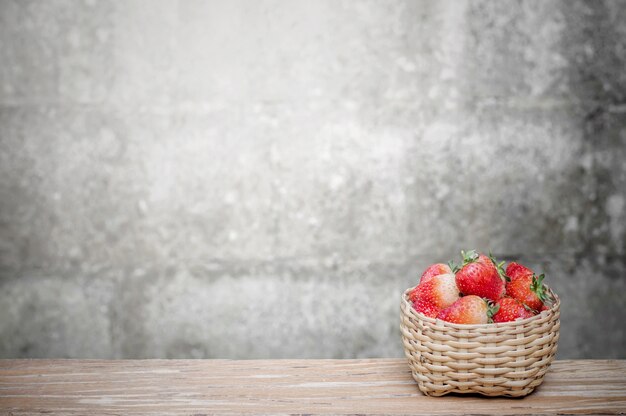 Fresh strawberry in bamboo basket on wooden table with old brick wall background 