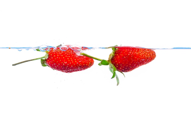 Fresh strawberry dropped into water with splash on white backgrounds