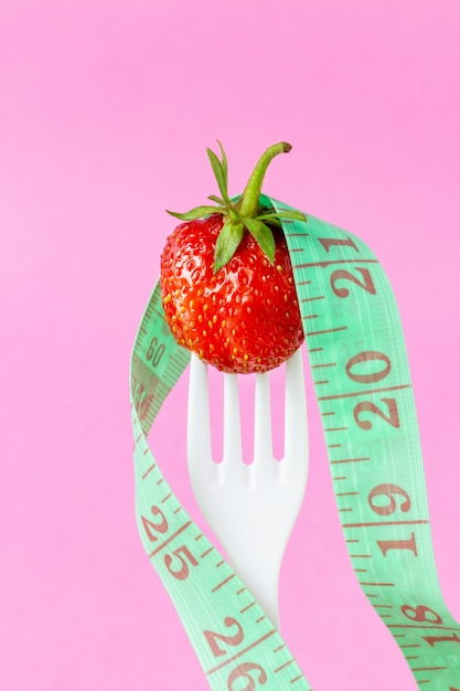 Fresh strawberry on white plastic fork with measuring tape