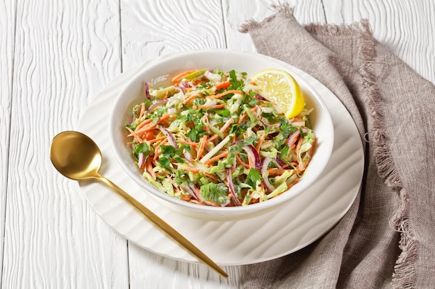 fresh summer coleslaw salad with light yogurt dressing in a white bowl on a wooden table