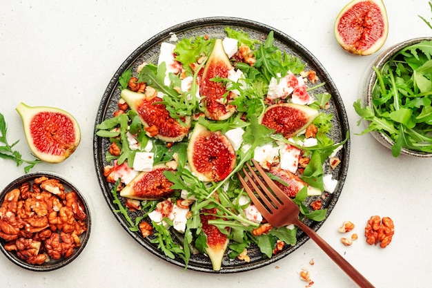 Fresh summer fig salad with white cheese nuts arugula and jam dressing on white table background top view copy space