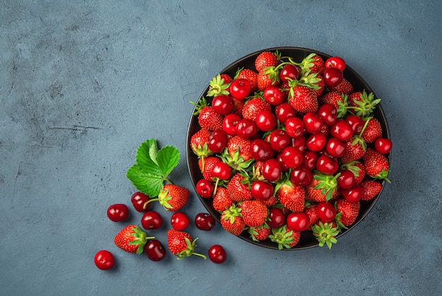 Fresh summer fruits and berries on a dark background. Juicy cherries and strawberries in a black plate.