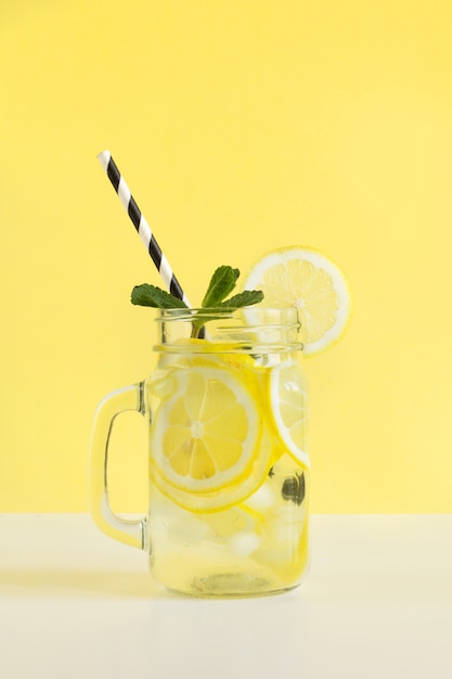 Fresh summer fruits water or lemonade with lemon and mint on yellow background. Close up.