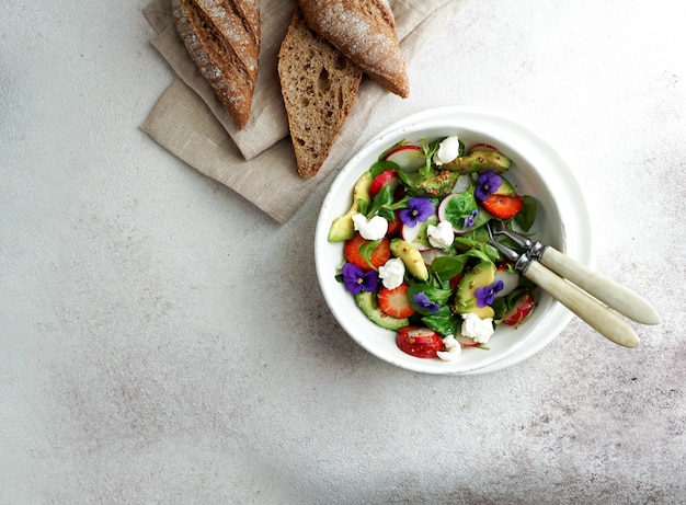 Fresh summer salad of arugula, avocado, radish and strawberries and edible flowers, olive oil