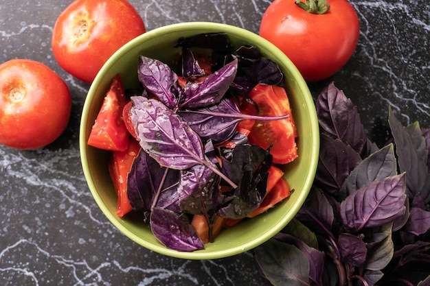 Insalata estiva fresca di pomodoro e basilico viola nella ciotola verde. vista dall'alto del cibo vegetariano