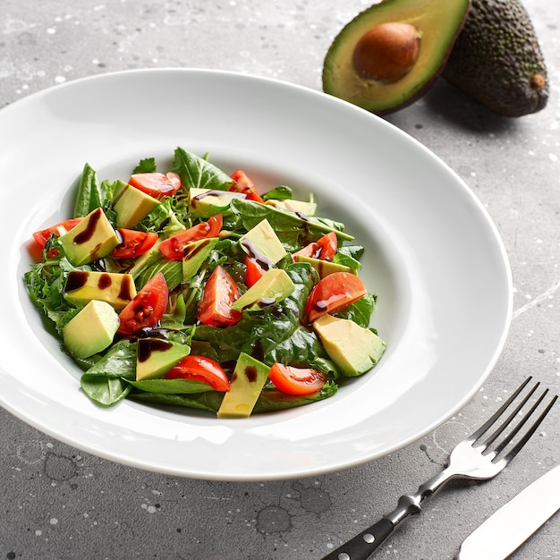 Fresh summer salad with avocado, lettuce, tomato and flax seeds on gray