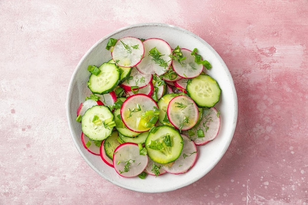 Insalata estiva fresca con cetrioli radicchio, cipolla, aneto e olio d'oliva in una ciotola su sfondo rosa vista dall'alto