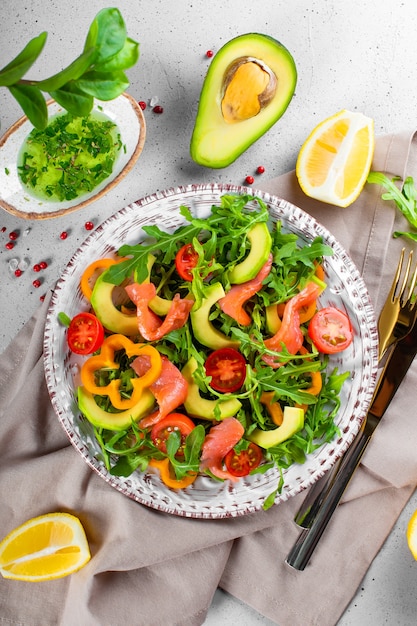 Insalata di verdure fresche estive con rucola, pomodori, peperoni, avocado e salmone su una foto verticale di vista dall'alto del piatto.