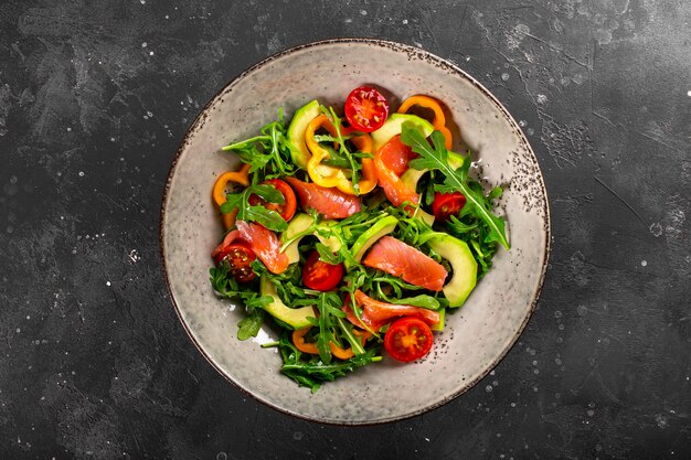 Fresh summer vegetable salad with arugula, tomatoes, bell peppers, avocado and salmon on a plate top view.