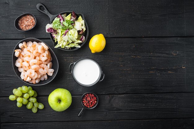 Fresh summer vitamin appetizer of green salad, shrimps, olive ingredients set, with sauce apple and grape, on black wooden table, top view flat lay