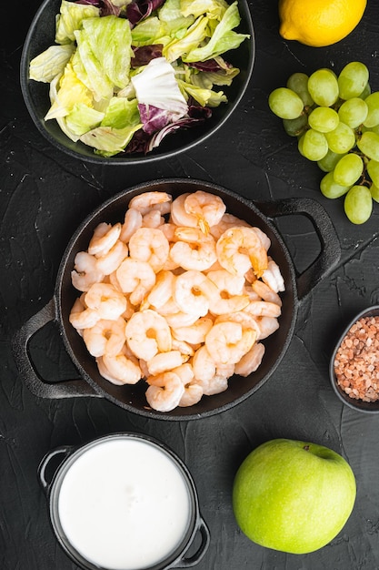 Fresh summer vitamin appetizer of green salad shrimps olive ingredients with sauce apple and grape on black stone background top view flat lay