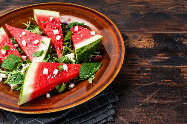 Fresh summer watermelon salad with feta cheese, arugula, onions in a rustic plate. Dark background. Top view. Copy space.