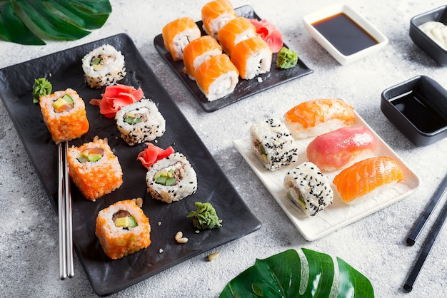 Fresh sushi set on black and white slate with metal sticks, sauce and green leaves