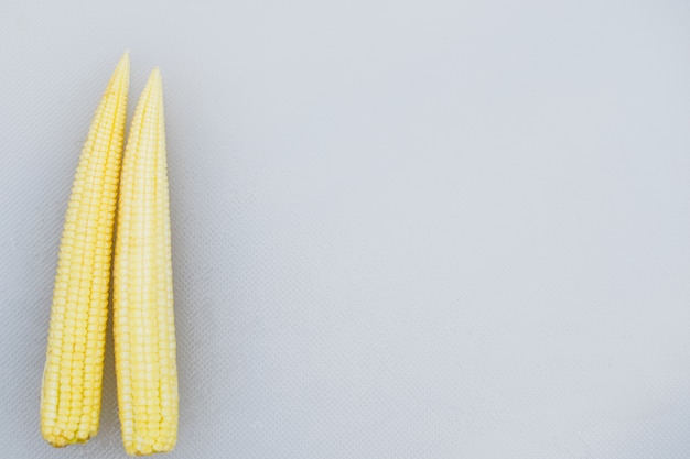 Fresh sweet baby corn on white plastic chopping block. 