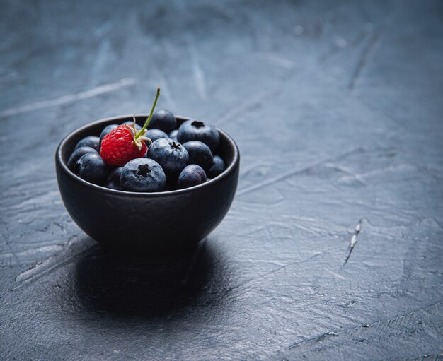 Fresh and sweet blueberry in  black  bowl with raspberry on dark.