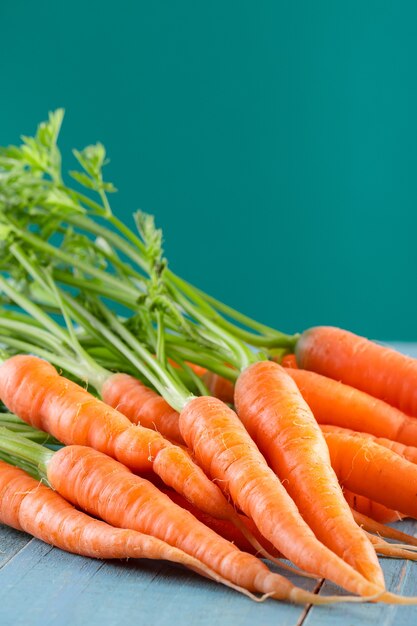Fresh and sweet carrots on a blue wooden table on greenish background