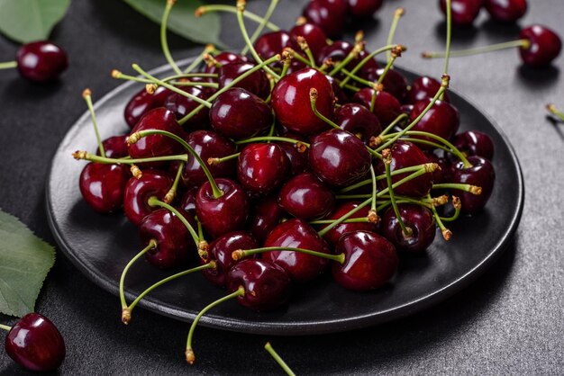 Fresh sweet cherries plate with leaves in water drops on stone background top view