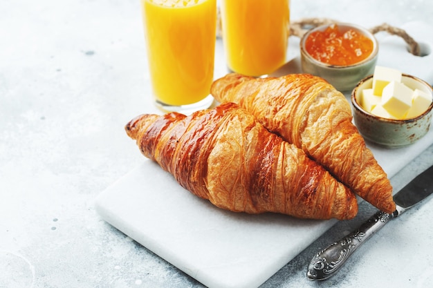 Fresh sweet croissants with butter and orange jam for breakfast. Continental breakfast on a white concrete table..