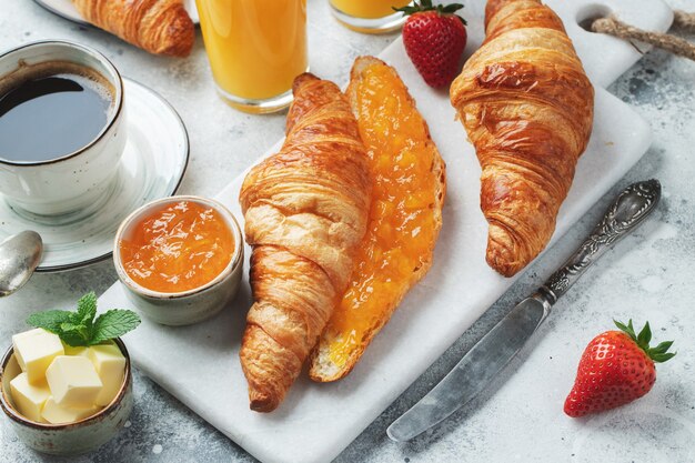 Fresh sweet croissants with butter and orange jam for breakfast.